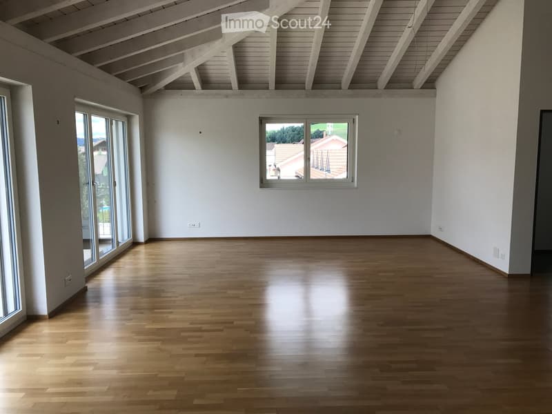 Empty room with wooden flooring, white walls, large windows, and a high, slanted wooden ceiling.