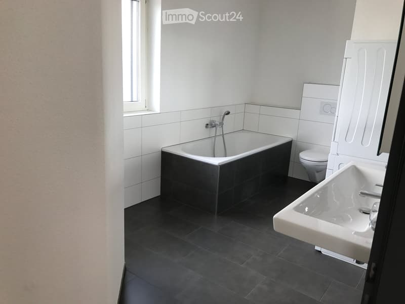 Modern bathroom with a black bathtub, white sink, and toilet. The walls are tiled in white and black, and the floor is dark grey.