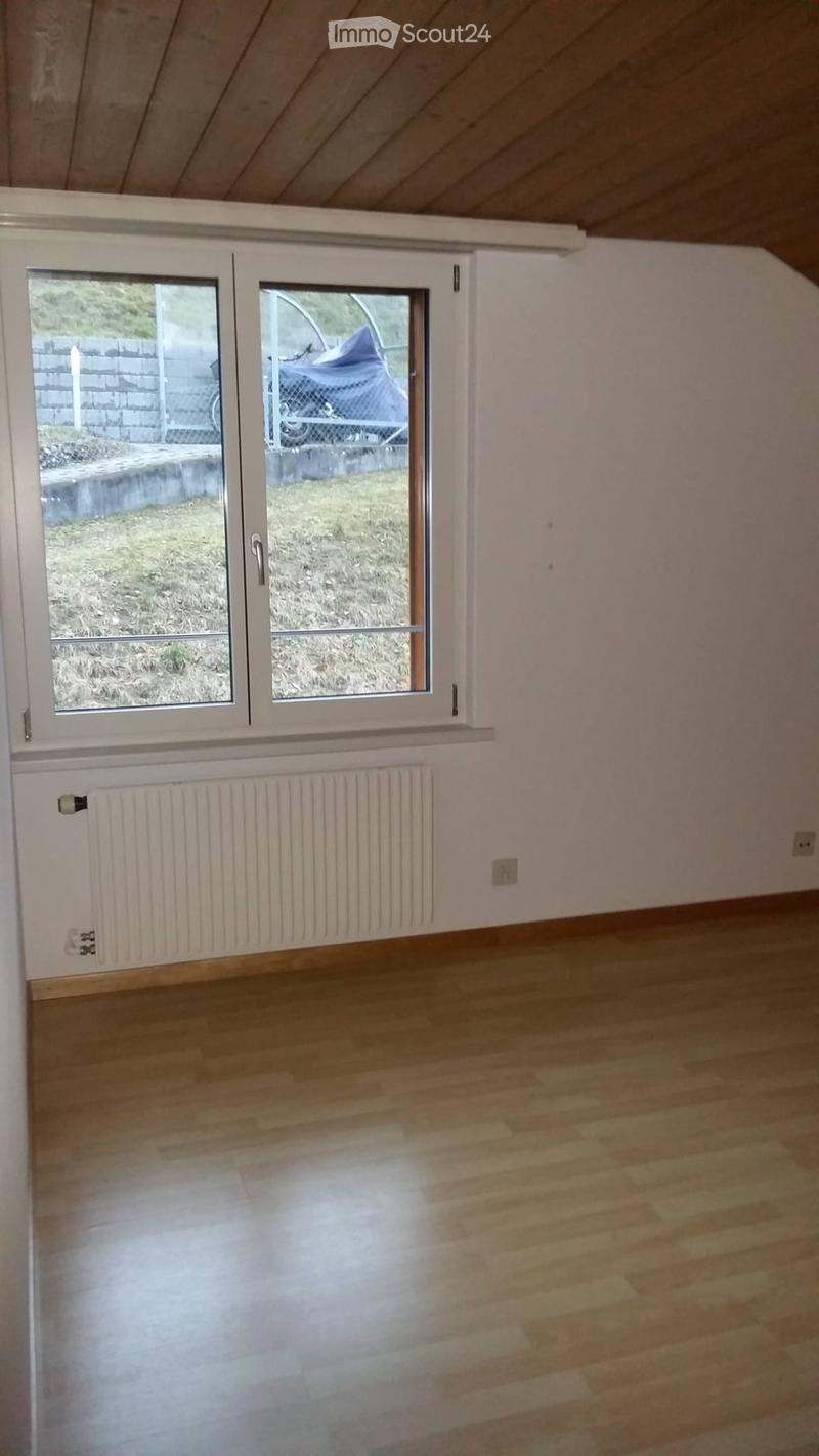 Empty room with wooden flooring, white walls, and a large window with a radiator below it.