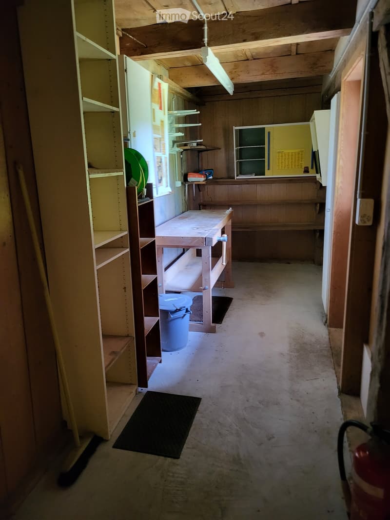 Empty hallway with wooden walls, exposed beams, shelves, and a workbench. No furniture or equipment.