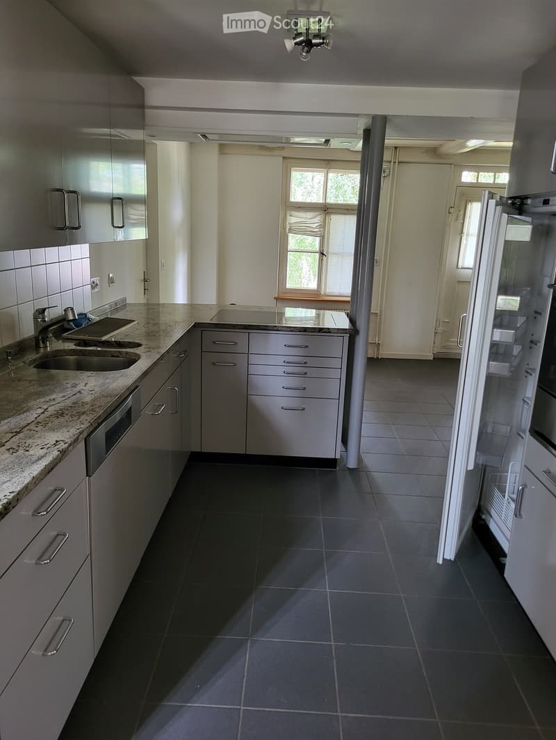 Modern kitchen with stainless steel appliances, granite countertop, and dark tiled floor.