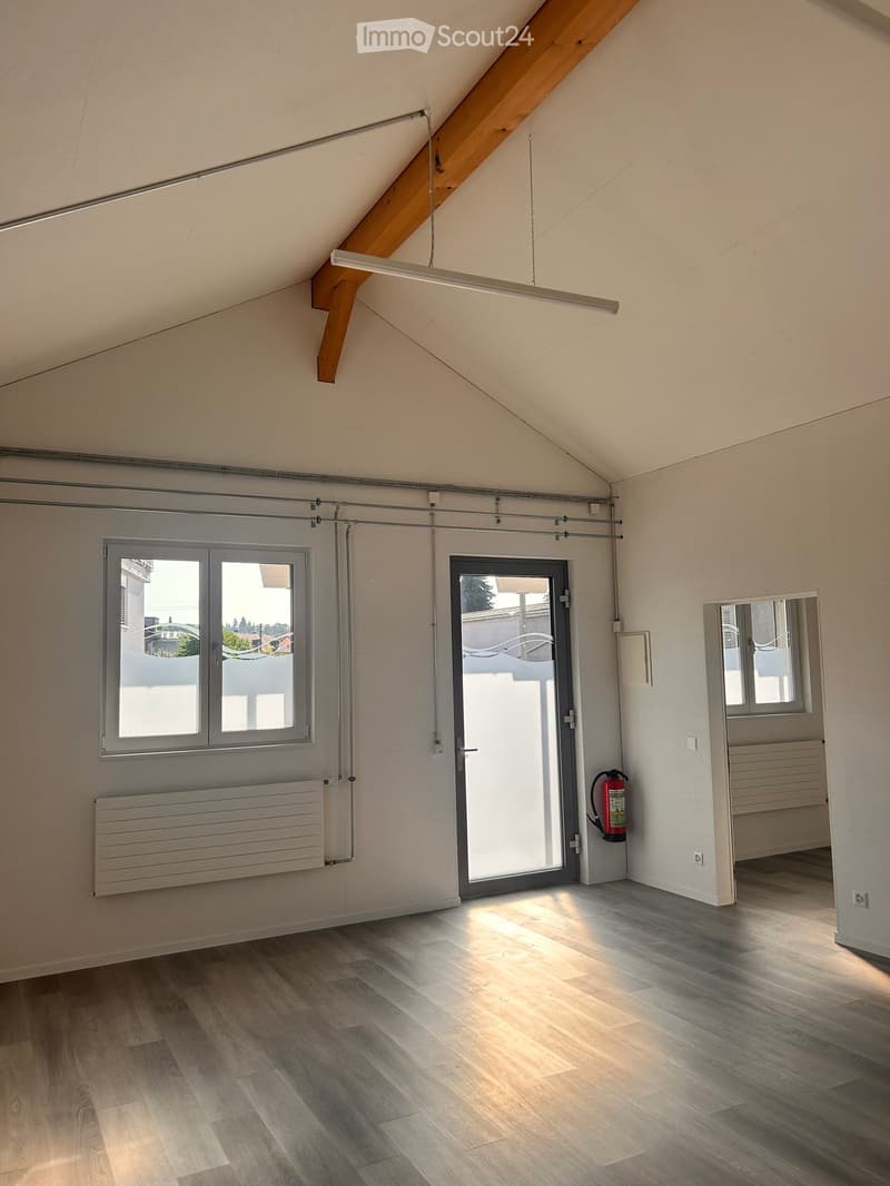 Empty attic room with wooden floor, white walls, large windows, sliding door, and exposed wooden beams on the ceiling.