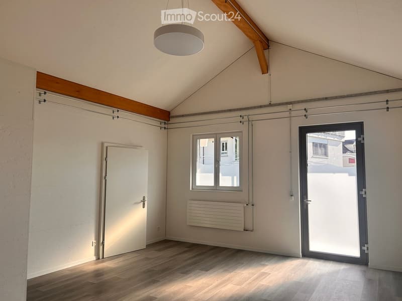 Empty room with wooden flooring, white walls, a large window, a sliding glass door, a radiator, and a hanging light fixture.