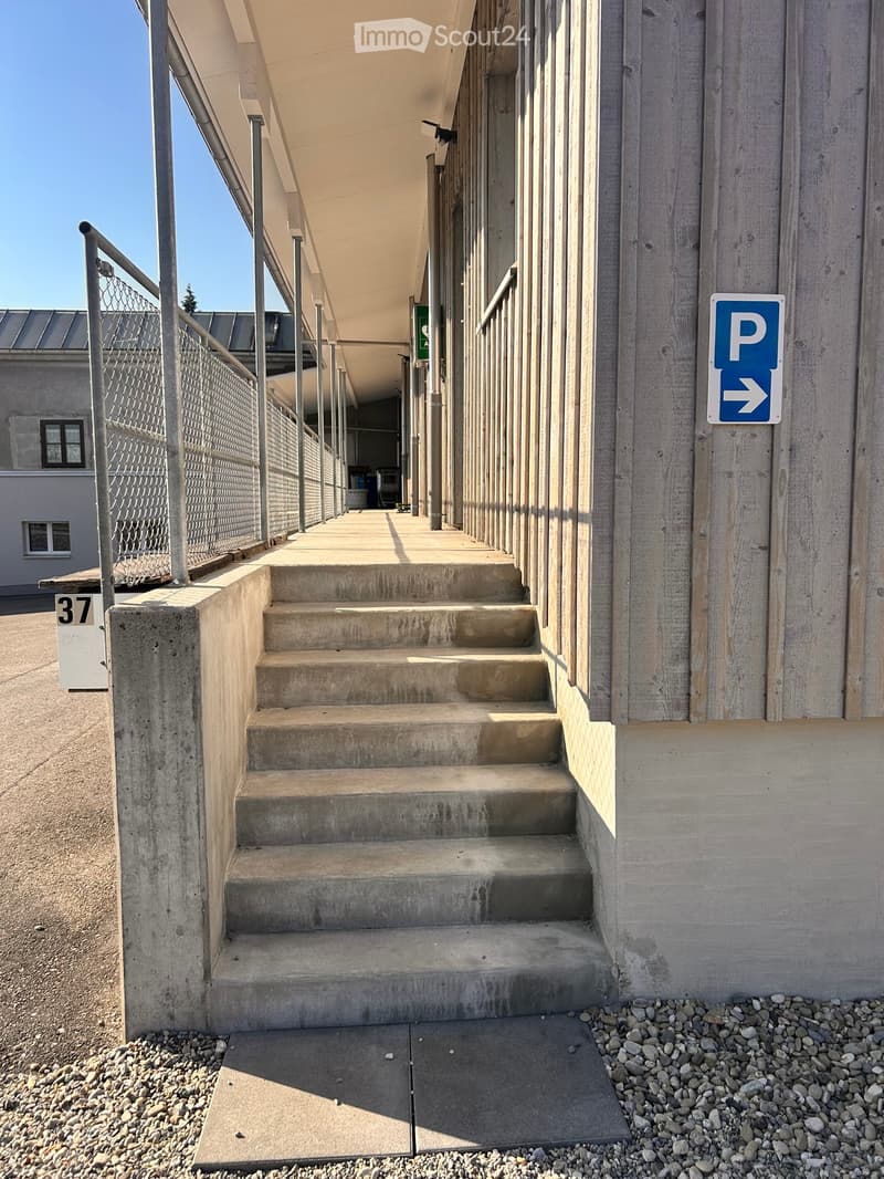 Concrete staircase leading up to a covered walkway with metal railings, adjacent to a building with a parking sign.
