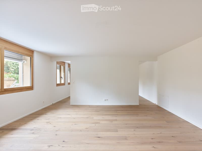 Empty room with light wooden flooring, white walls, and large windows with wooden frames. No furniture or equipment present.