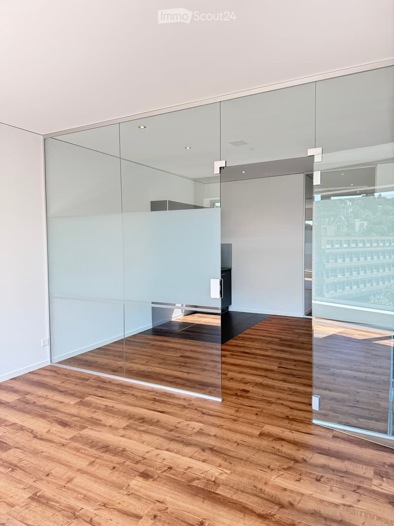 Empty room with wooden flooring, glass partitions, and white walls. No furniture or equipment visible.