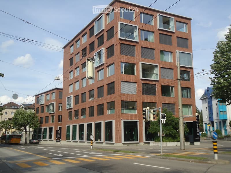 modern multi-story building, brick facade, glass windows, balconies, ground-level storefronts, overhead power lines