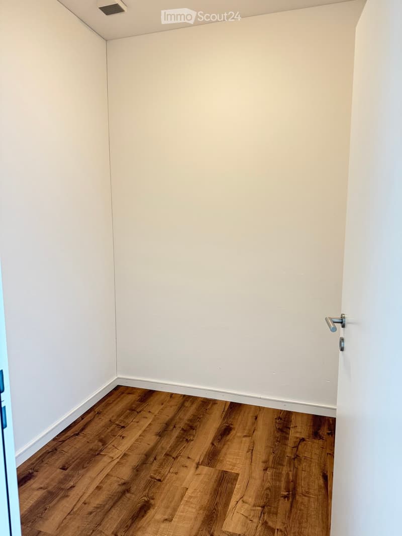 Empty room with light-colored walls and wooden flooring, featuring a door handle on the right side.