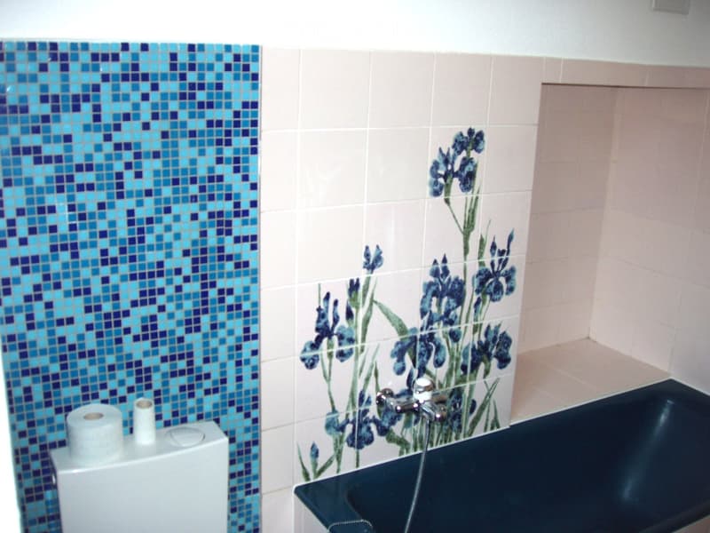 Bathroom with blue mosaic tiles on one wall, floral-patterned tiles on another, a toilet paper holder, and a black sink with a chrome faucet.