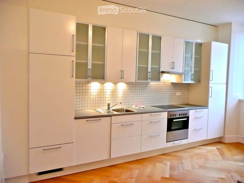 Modern kitchen with white cabinets, stainless steel sink, oven, and tiled backsplash.