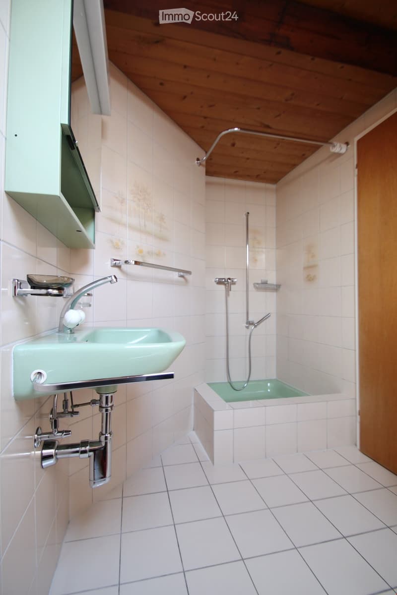 Bathroom with white tiles, green sink, shower area, and wooden ceiling.