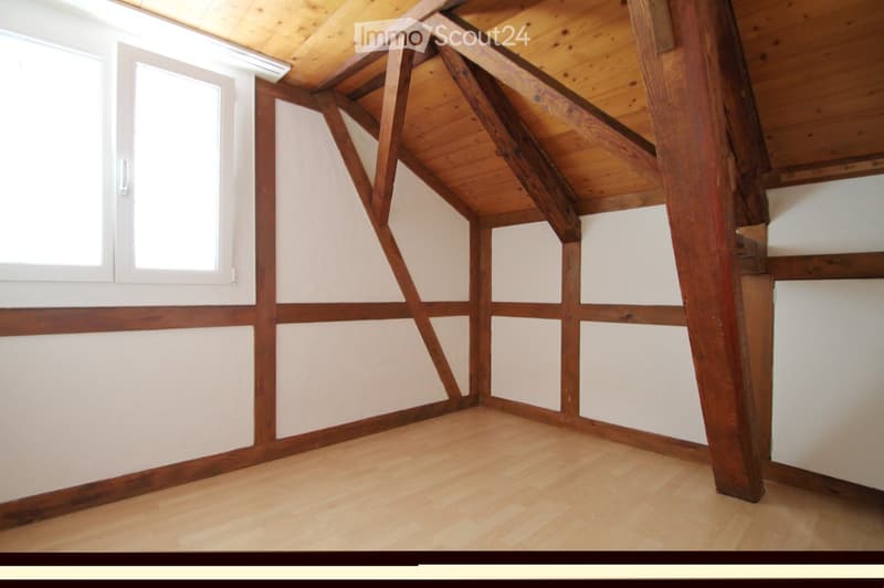 An empty room with wooden beams, white walls, and wooden flooring. There are two windows on the left side.