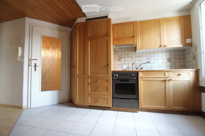 A kitchen with wooden cabinets, a white door, and a tiled wall. It features an oven, a sink with a faucet, and a tiled backsplash.