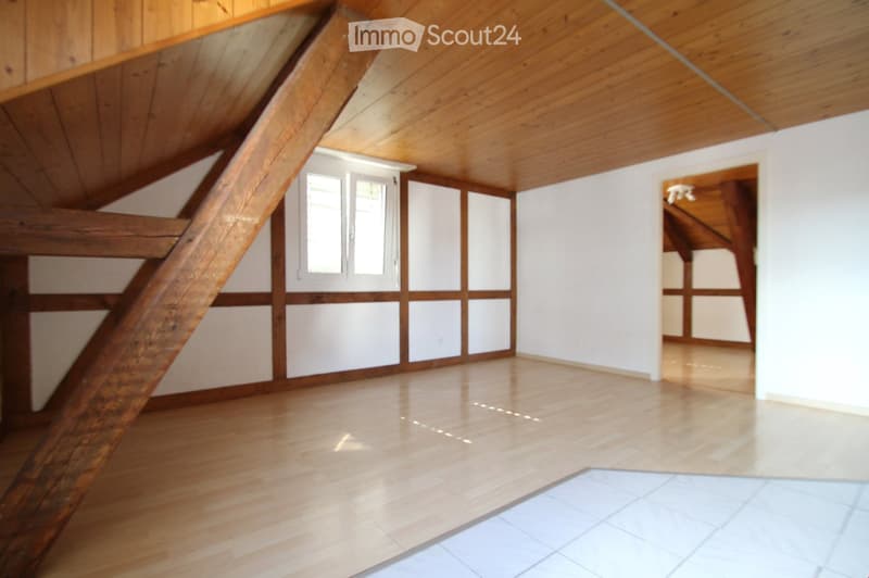 Empty attic room with wooden beams, white walls, and wooden floor. No furniture or equipment.