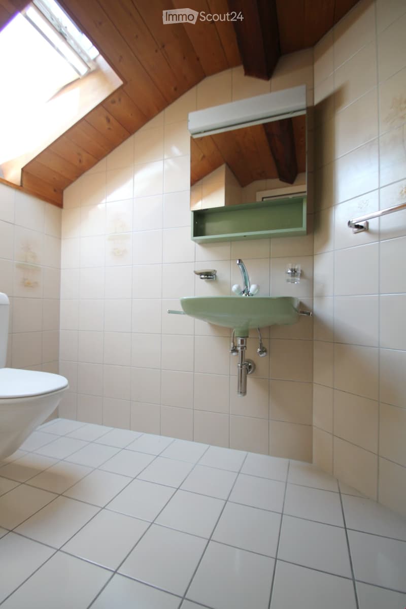 Bathroom with white tiles, wooden ceiling, white toilet, green sink, mirror, and towel rack.