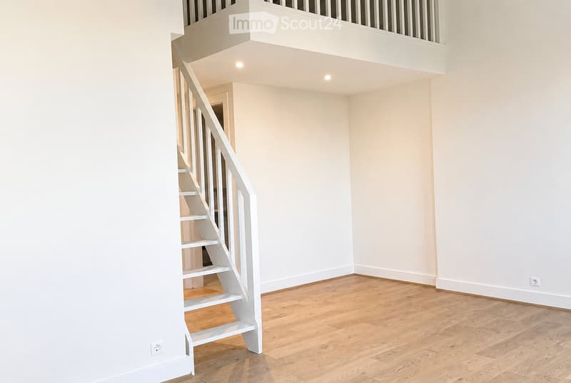 Empty room with light wooden flooring and white walls, featuring a white staircase leading to an upper level.