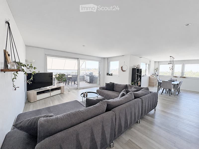 Modern living room with a grey sectional sofa, coffee table, TV, dining area, and balcony access.