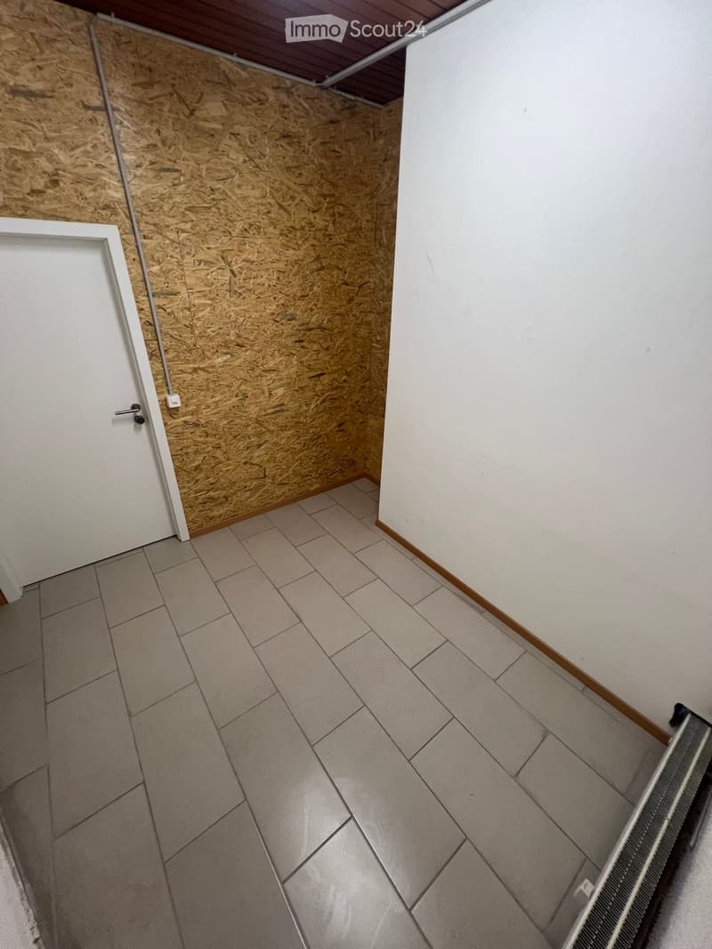 Empty room with tiled floor, white walls, and a wooden panel wall section. No furniture or equipment present.