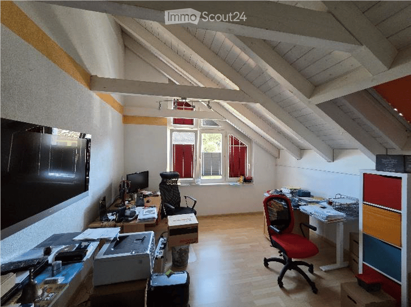 Office space with wooden flooring, slanted ceiling beams, large windows, desk with office equipment, chairs, and storage cabinet.