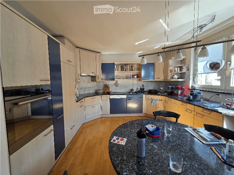 Modern kitchen with white and blue cabinets, granite countertop, built-in oven, sink, and various kitchen utensils. A round dining table with chairs is placed in the center.