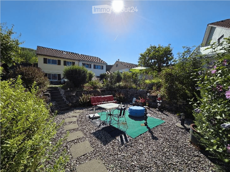A sunny garden area with a patio, outdoor furniture, and a house in the background.