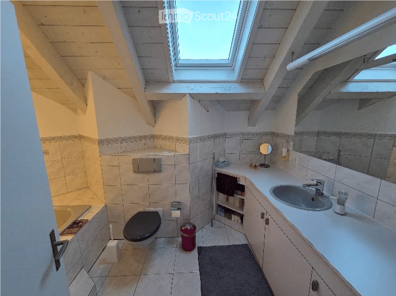 Bright bathroom with white tiled walls and floor, a large skylight window, a sink with a mirror, a toilet, a bathtub, and a small cabinet with towels and toiletries.
