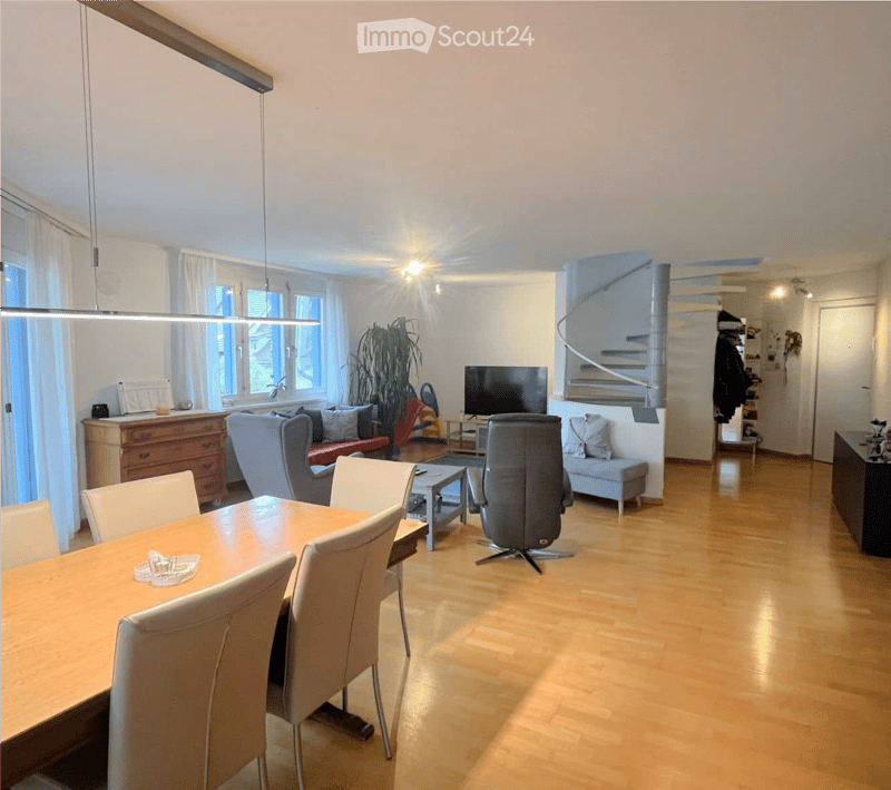 Bright living and dining area with wooden flooring, large windows, a sofa, dining table with chairs, a television, and a plant. A spiral staircase leads to another level.