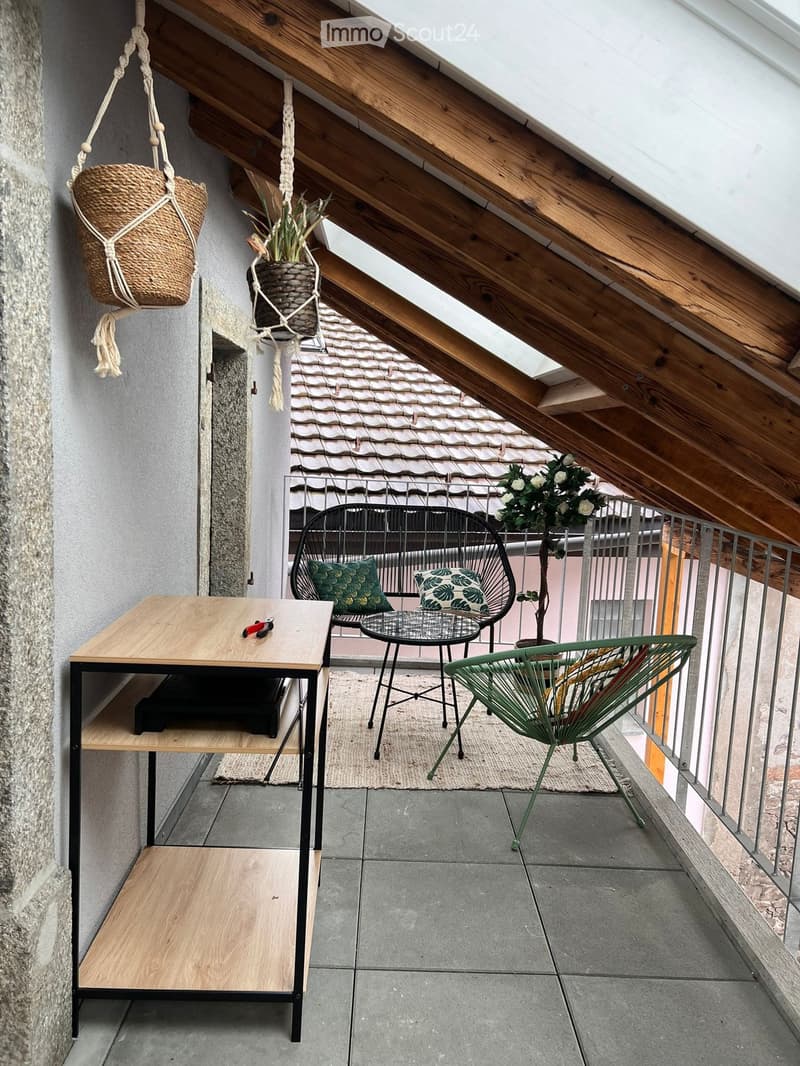 Balcony with wooden table, metal chairs, potted plants, and hanging baskets.