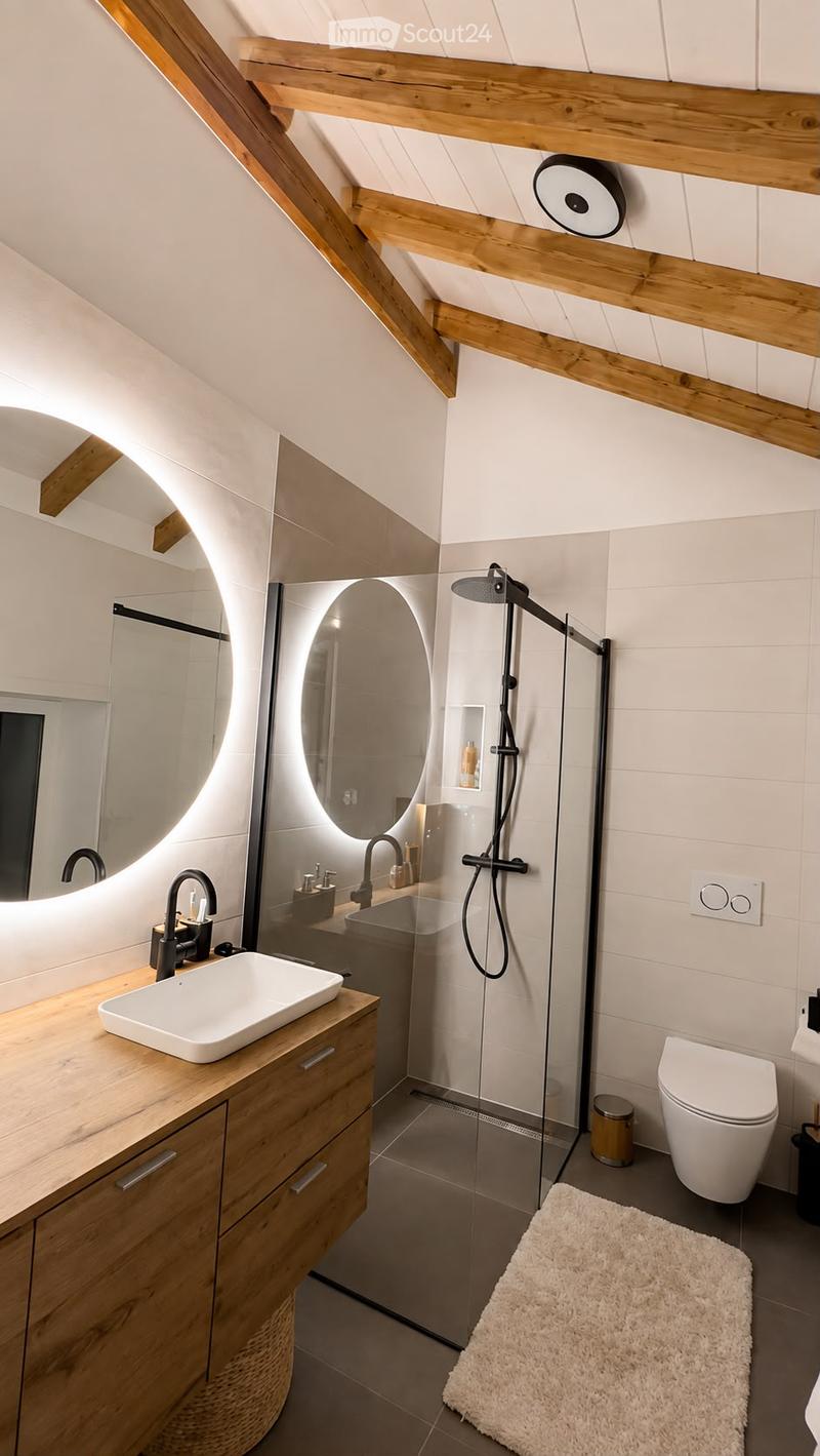 Modern bathroom with wooden beams, white sink, round mirror, glass shower enclosure, and sleek fixtures.
