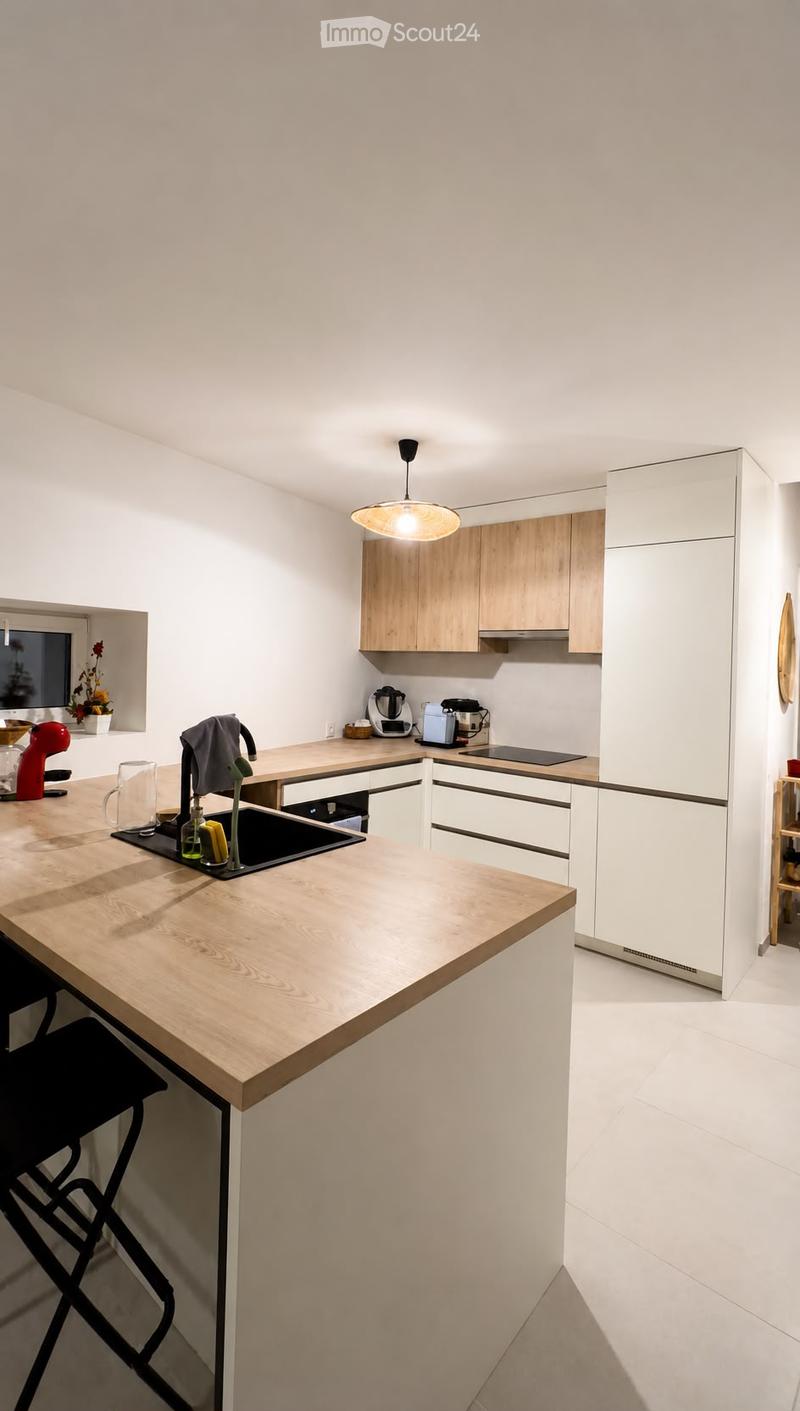 Modern kitchen with light wooden countertops, white cabinets, and stainless steel appliances. Features a central island with a sink and various kitchen items.