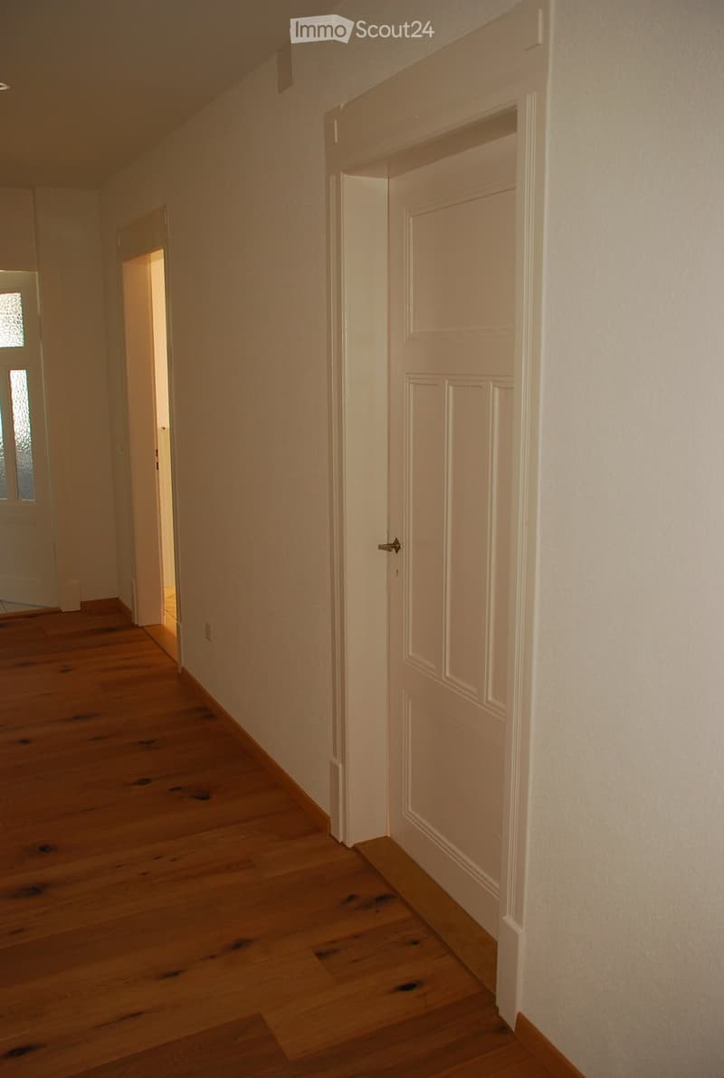 Empty hallway with wooden flooring, white walls, and closed doors on both sides.