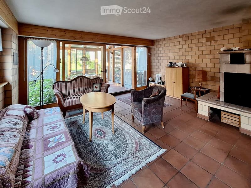 Cozy living room with tiled floor, brick walls, fireplace, sofa, armchair, coffee table, and large windows leading to a patio.