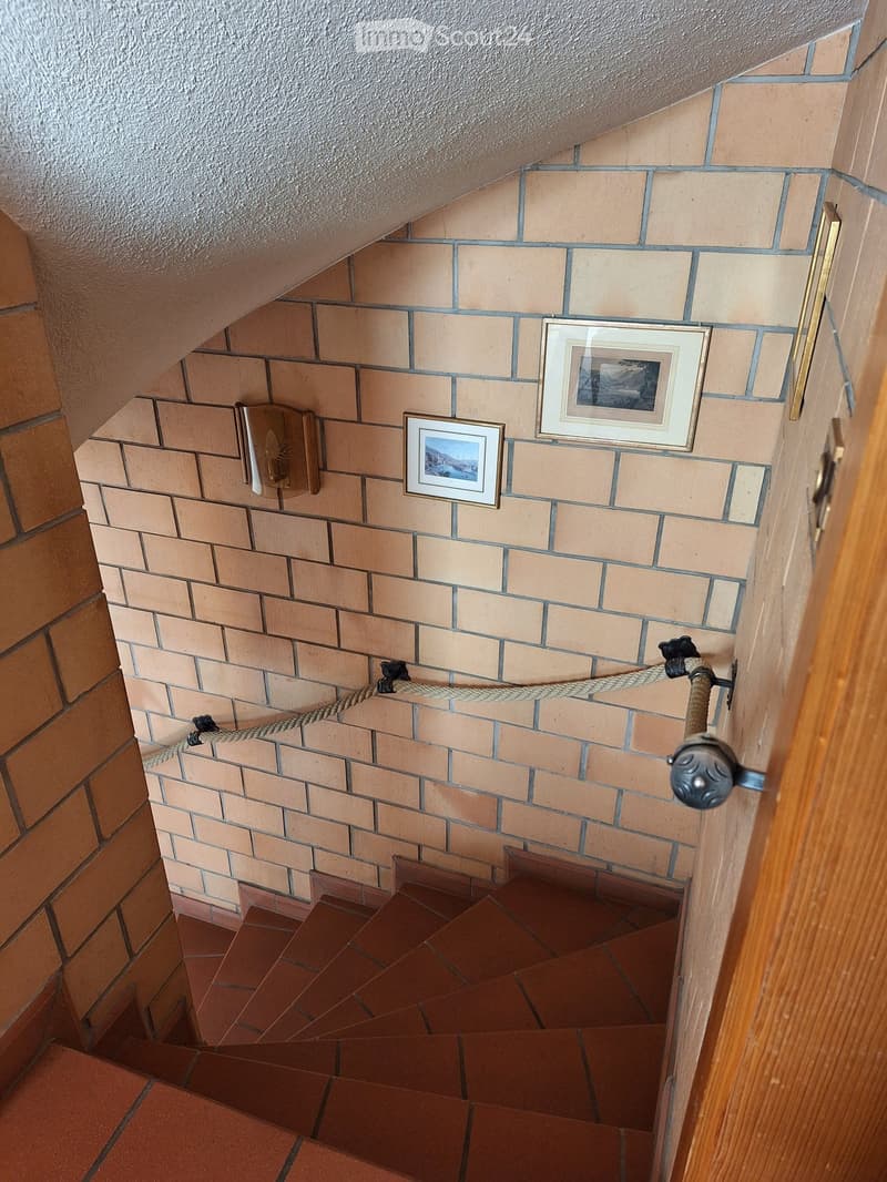 Staircase with red tiles, beige brick walls, rope handrail, and framed pictures on the wall.
