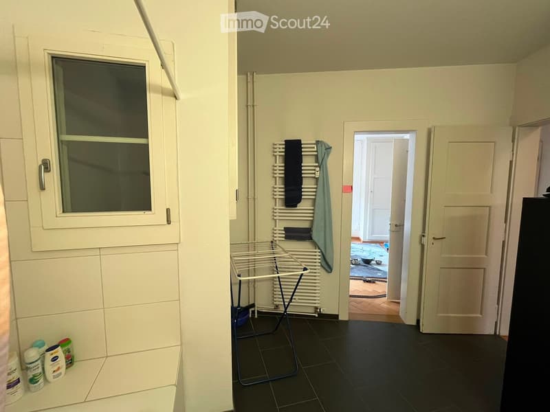 Bathroom with dark tiled floor, white radiator, towel rack with a towel, and a small shelf with toiletries near the window.