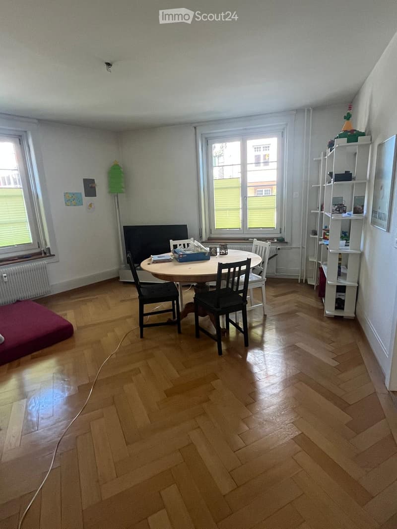 Dining room with wooden floor, round table, four chairs, white shelving unit, and a flat-screen screen.