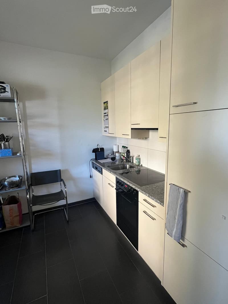 Modern kitchen with white cabinets, black tiled floor, granite countertop, sink, oven, and a chair near the counter.