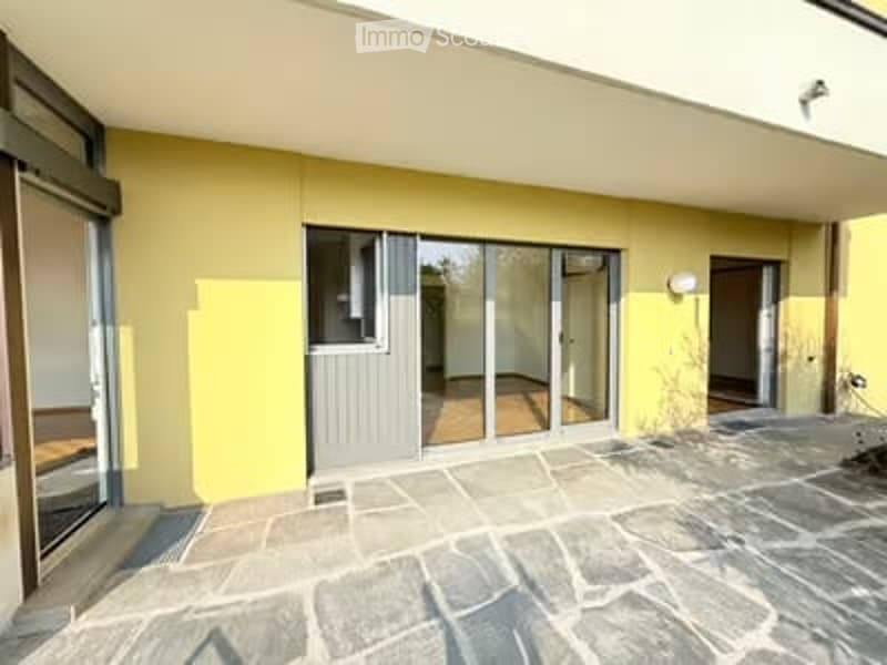 Outdoor patio area with stone flooring, large sliding glass doors leading to interior, yellow walls, and a small seating area visible through the glass.
