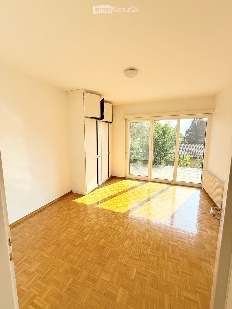 Empty room with wooden herringbone flooring, white walls, large sliding glass doors leading to a balcony, and a small built-in cabinet.