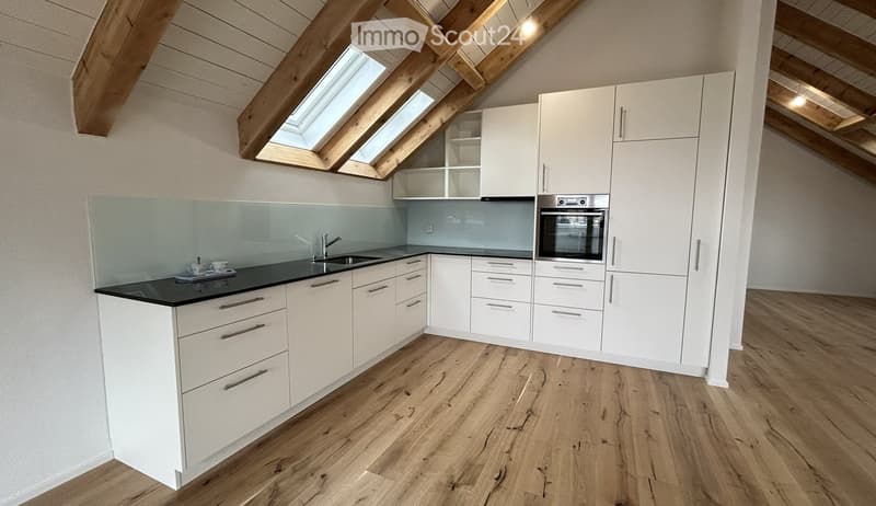 Modern kitchen with white cabinets, black countertop, wooden flooring, and built-in appliances including an oven and sink.