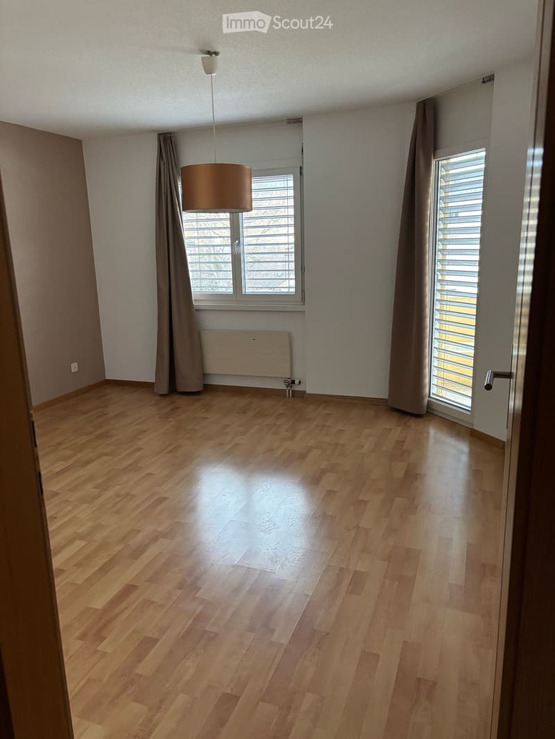 Empty room with wooden flooring, large windows with blinds, and a radiator. No furniture or equipment present.