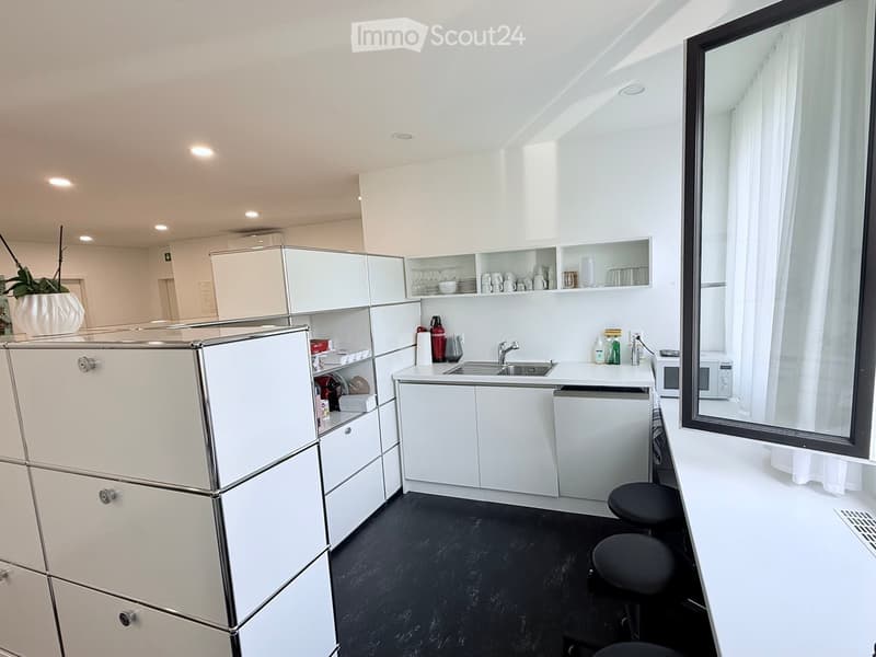 Modern kitchen with white cabinets, stainless steel sink, microwave, and stools.