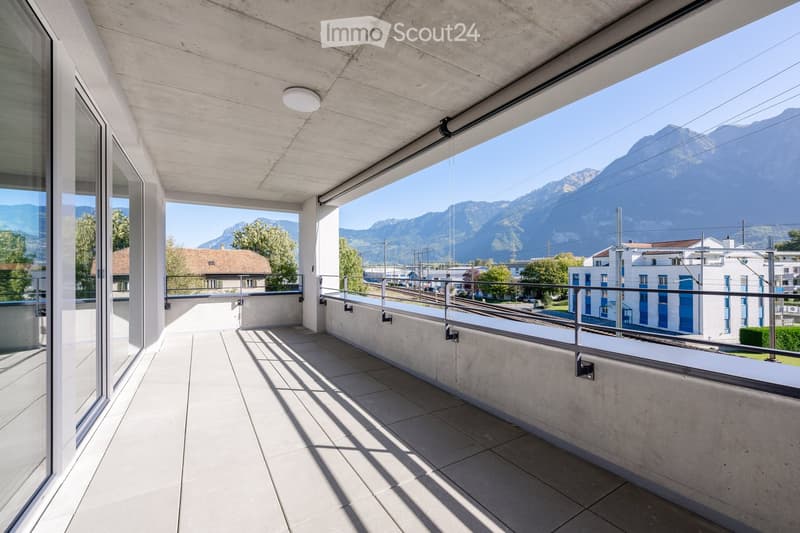 Modern balcony with concrete floor, glass walls, and metal railing, offering a scenic mountain view.