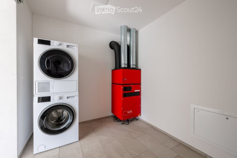 A small utility room with a white washing machine, dryer, and a red boiler unit with two vertical pipes.