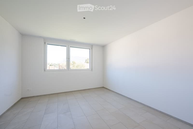 Empty room with white walls, tiled floor, and large windows offering a view of the outside.