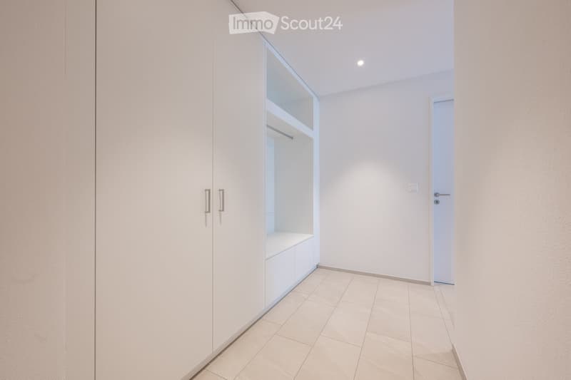 Empty hallway with white walls, tiled floor, built-in closet with mirrored doors, and a closed door at the end.