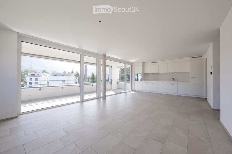 Bright, open-plan space with large glass sliding doors leading to a balcony, white tiled floor, and white cabinetry in the adjacent kitchen area.