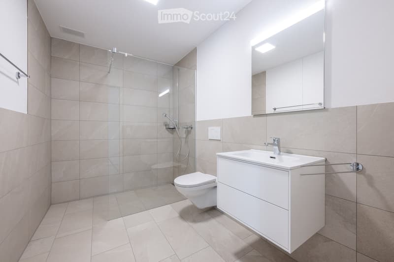 modern bathroom with glass shower, white sink, white toilet, white cabinets, tiled floor, tiled walls