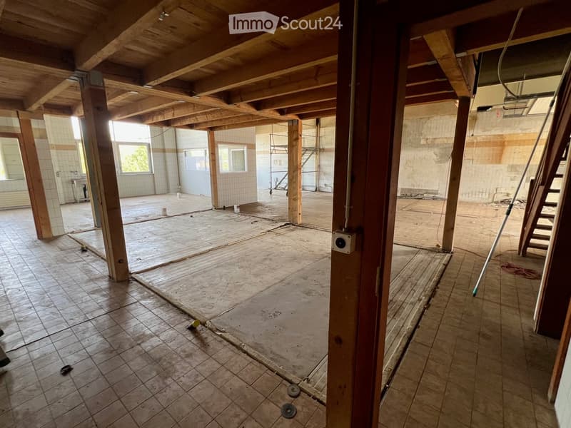 Empty room with exposed wooden beams, tiled floor, and large windows. No furniture or equipment present.
