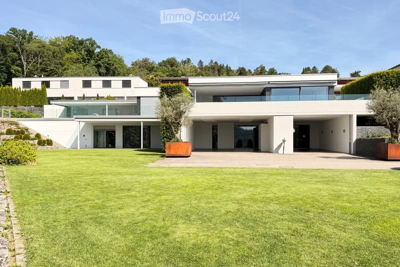 Modern two-story house with white exterior, large windows, and a spacious lawn in front.