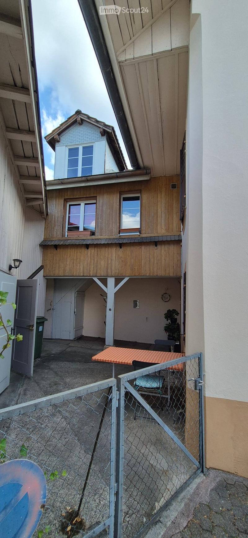 Courtyard with a small table, chairs, and potted plants, enclosed by a metal fence.